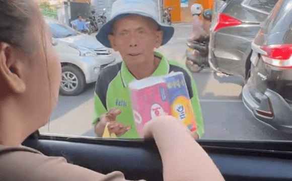Bapak penjual tisu menunjukkan bungkus tisunya ke arah jendela mobil saat berinteraksi dengan Jestham di jalanan.